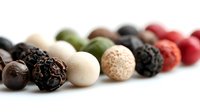 Colorful assortment of peppercorns in row including black, white, green, and pink varieties on white background, macro food photography for culinary design.