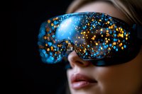 Young Caucasian woman wearing protective glasses with magical blue and gold bokeh light reflections on dark background, close up view of face and eyewear.
