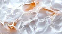 Macro shot of melting ice cubes with orange tinted liquid creating abstract patterns and textures, bubbles and droplets on frosty crystalline surface in cold environment.