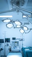 Modern hospital operating room with surgical LED lights overhead, medical equipment and monitors in sterile blue-toned environment.
