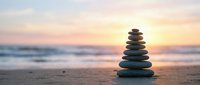 Zen stone stack on beach at sunset with soft waves and golden sky creating peaceful meditation atmosphere for wellness and mindfulness practices.