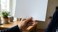 Senior male with dark skin tone holding blank white paper sheet indoors, suitable for advertising, marketing campaigns, presentations, and promotional materials.