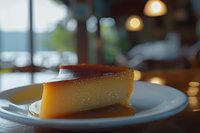 Creamy caramel flan dessert slice on white plate in cozy restaurant setting with warm ambient lighting and blurred background creating inviting dining atmosphere.