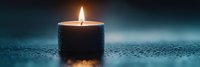 Single burning candle with warm glowing flame against dark teal background, creating peaceful ambiance. Water drops and bokeh add mystical atmosphere.