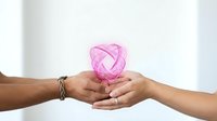 Two hands gently holding glowing pink breast cancer awareness ribbon symbol together in supportive gesture for healthcare campaign and solidarity.