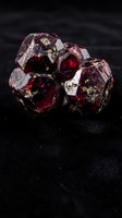 Raw red garnet crystal cluster with natural faceted surfaces and golden inclusions on dark background for jewelry making and mineral collection displays.