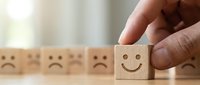 Hand selecting wooden cube with happy face from row of sad face blocks representing positive mindset choice and emotional well-being transformation.