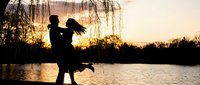 Romantic couple silhouette embracing by lake at golden sunset with weeping willow tree, perfect for love and relationship themed designs.