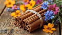 Aromatic cinnamon sticks tied with twine alongside vibrant wildflowers including yellow cosmos and blue cornflowers on rustic wooden background, macro food photography.