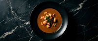 Creamy tomato soup with fresh herbs and croutons served in elegant black bowl on dark marble surface for gourmet dining and restaurant menu photography.