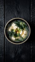 Traditional Japanese miso soup with tofu cubes and wakame seaweed in ceramic bowl on dark wooden table for authentic Asian cuisine and healthy dining.