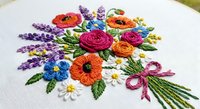 Colorful hand embroidered floral bouquet with roses, poppies, lavender and daisies on white fabric. Traditional needlework craft for home decor projects.