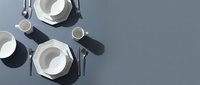 Overhead view of elegant table setting with white plates, silverware, and glasses arranged on gray surface for fine dining or event planning.