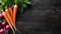 Fresh organic carrots and red radishes with green tops on dark rustic wooden background, copy space for menu or recipe design.