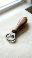 Bottle opener with wooden handle resting on neutral linen surface near window, suitable for kitchen, hospitality, and product photography.