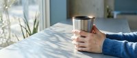 Cozy morning moment with hands holding warm coffee mug at sunny kitchen table creating peaceful atmosphere for relaxation and mindfulness.