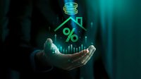 Businessman holding glowing holographic house with percentage symbol and coins above palm representing mortgage rates and real estate investment concepts.