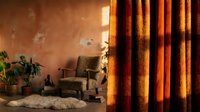 Warm-toned interior space featuring golden orange curtains, vintage armchair, potted plants, and textured terracotta walls with natural light for home decor and design projects.