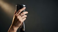 Hand holding vintage microphone with dramatic lighting for music recording and performance applications.