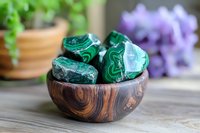 Green malachite stones in wooden bowl on rustic table with blurred potted plants background, healing crystals for meditation and spiritual practice.