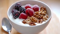 Fresh raspberries and blackberries with crunchy granola in creamy yogurt bowl, served for healthy breakfast on wooden table. Natural morning light.