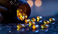 Soft-focus macro shot of amber fish oil omega-3 gel capsules spilling from dark bottle onto reflective surface with blurred bokeh lights in background.