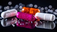 Colorful medical pills and capsules on reflective black surface with bokeh lights background, pharmaceutical concept with pink, white and orange medicine.
