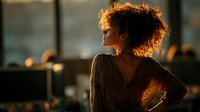Young African American woman with curly hair in warm golden light looking away thoughtfully in modern office environment for business and lifestyle concepts.