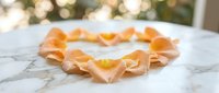 Heart-shaped arrangement of delicate peach rose petals on white marble surface with warm bokeh lights creating romantic atmosphere for wedding decor.