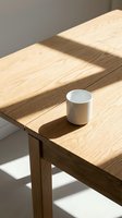 White ceramic mug on wooden table with natural sunlight casting shadows, minimalist workspace setup for coffee, beverage, or product mockup designs.