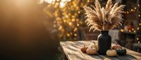 Cozy autumn home decor with pampas grass in dark vase, small pumpkins on wooden table against warm bokeh lights creating seasonal atmosphere for fall interior design.