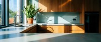 Modern minimalist kitchen with wooden island, concrete countertops, and natural light from large windows. Potted plant adds greenery to contemporary interior design space.