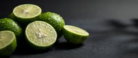 Fresh green limes cut in half showing juicy pulp on dark slate surface for culinary cooking recipes and citrus fruit photography backgrounds.