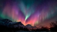 Spectacular aurora borealis with vibrant pink and green lights dancing over snow-capped mountain range at night, creating magical atmospheric phenomenon.