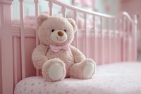 Pink teddy bear with bow sitting on polka dot bedding against nursery crib, soft focus romantic lighting creates gentle dreamy atmosphere for baby room decor.