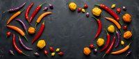 Colorful hot chili peppers and small tomatoes arranged in decorative pattern on dark slate background. Spicy vegetables for cooking and culinary design projects.