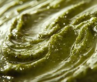 Closeup of green cosmetic paste or clay mask with swirled texture and water droplets, suitable for skincare, beauty, and wellness product packaging and marketing materials.