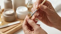 Woman applying cuticle oil with dropper bottle during professional manicure treatment in spa salon with cosmetic jars and wooden tools on table.