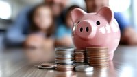 Pink piggy bank with stacked coins on table with blurred family background representing savings, financial planning and money management for future goals.
