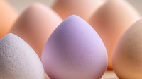 Macro shot of makeup beauty blender sponges in soft pastel colors against blurred background, showing textured surface detail and gentle curves.