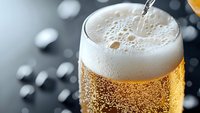 Fresh cold beer being poured into glass with rising bubbles and thick white foam head against dark background, macro close-up shot showing golden liquid texture.