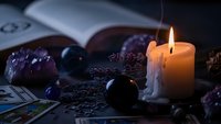 Mystical fortune telling setup with burning candle, tarot cards, crystal ball and amethyst stones creating atmospheric divination scene for spiritual guidance.