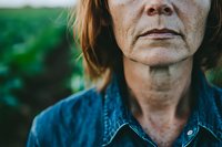 Close up portrait of mature woman wearing denim jacket against green natural background, showing natural aging skin texture and authentic expression.