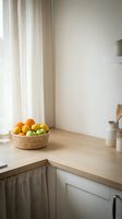 Bright kitchen counter with woven basket filled with fresh oranges and apples, natural light from window, minimalist Scandinavian interior design, wooden countertop, white cabinetry.