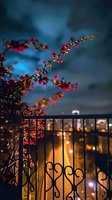 Pink blossoms on branch overhanging decorative metal fence at dusk, with soft bokeh lights creating romantic atmosphere against dark blue evening sky.