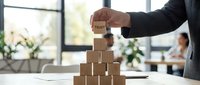 Business professional building wooden block pyramid with trust concept in modern office environment for corporate leadership and team development strategies.