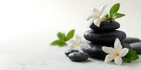 Zen spa composition with stacked black massage stones and delicate white jasmine flowers on light background, creating tranquil atmosphere for wellness treatments.