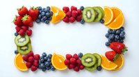 Fresh colorful fruit frame with strawberries, blueberries, raspberries, kiwi and orange slices arranged in border on white background for healthy eating.