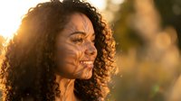 Young mixed-race woman with curly hair in golden sunlight with natural shadows on face during sunset outdoors creating warm atmospheric portrait.