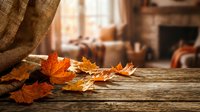 Autumn leaves scattered on rustic wooden table with warm sunlight streaming through window creating cozy seasonal atmosphere for fall decorating.